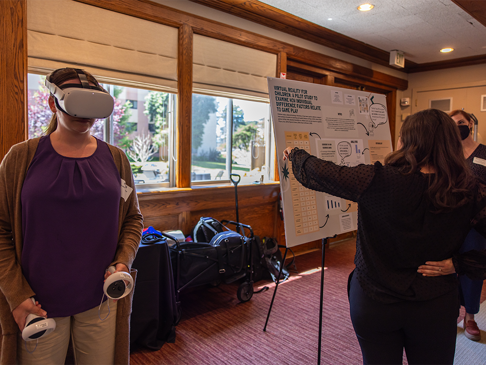 Someone wearing a VR headset next to a research poster at CHSS showcase