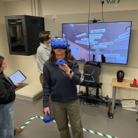 students working in VR with a headset, laptop, and large display