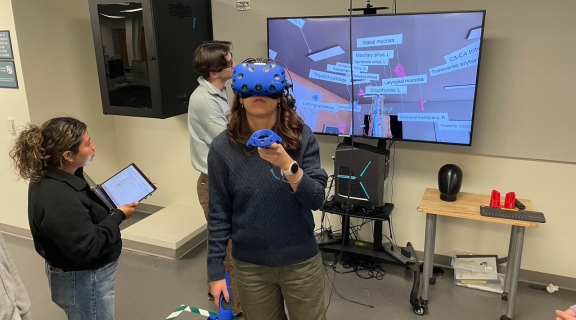 students working in VR with a headset, laptop, and large display